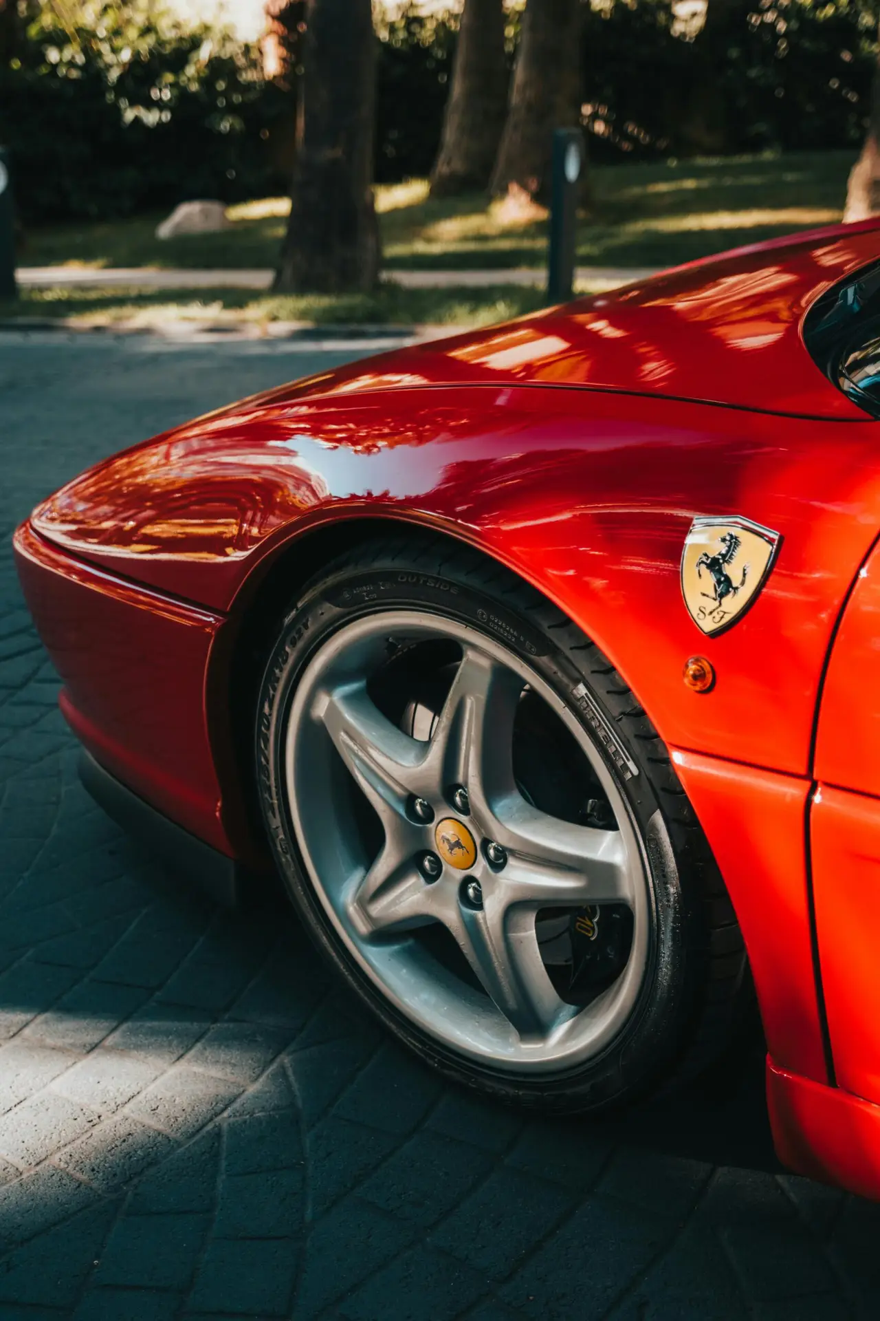 A striking close-up of a red Ferrari showcasing its wheel and emblem in a sunny outdoor setting.