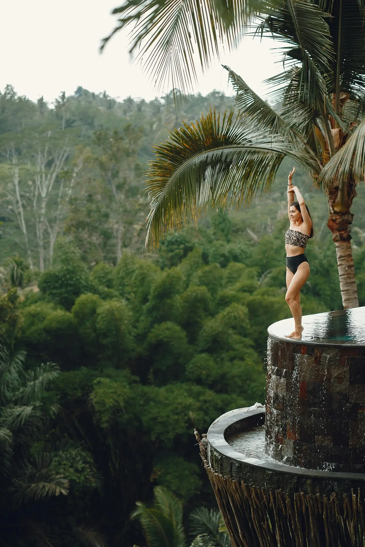 Woman in swimwear gracefully posing by an infinity pool amidst tropical scenery, capturing vacation bliss.