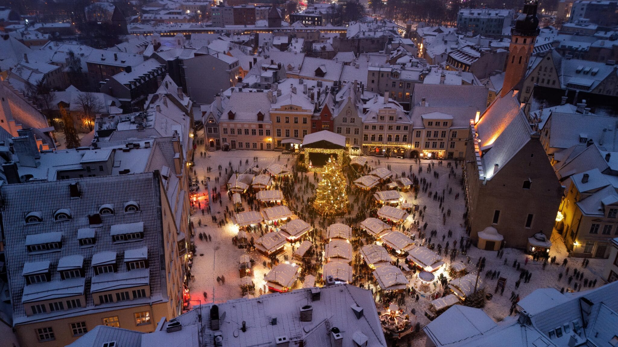 Plaza del Ayuntamiento de Tallin nevada con mercado navideño y árbol iluminado