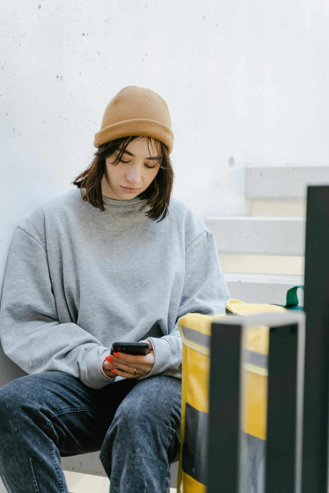 Una persona sostiene el teléfono junto a una ventana; la luz fría sugiere la espera y el peso de un silencio digital.